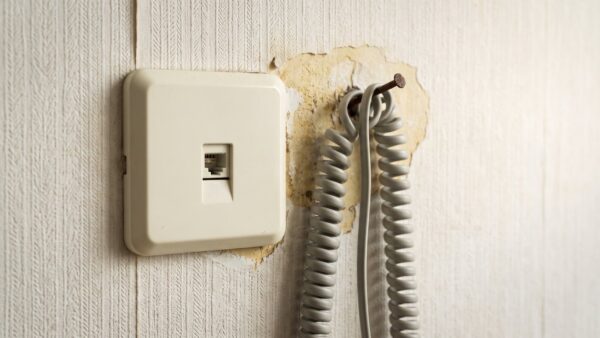 telefonanschluss umstellung bild 1 Alte unbeschriftete Telefonanschlussdose an einer Raufasertapete mit aufgerolltem Kabel
