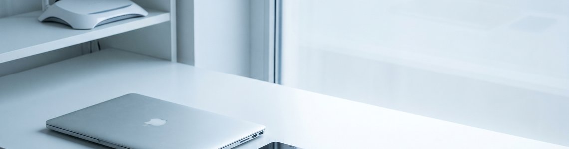 Schreibtisch mit zugeklapptem Laptop, Smartphone, Schlüsselbund und weißem Router im Regal