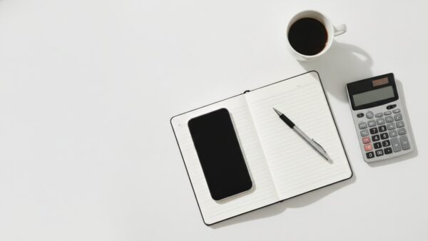 telekom rueckgabedeal bild 2 Smartphone, Notizblock und Taschenrechner auf einem Schreibtisch beim Nachrechnen der Handy-Finanzierung