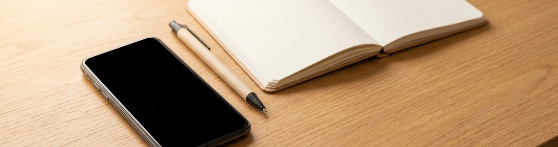 Smartphone mit schwarzem Bildschirm und leeres Notizheft auf einem Schreibtisch