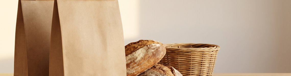 Unbedruckte Papiertueten mit Brot auf einem hellen Holztresen