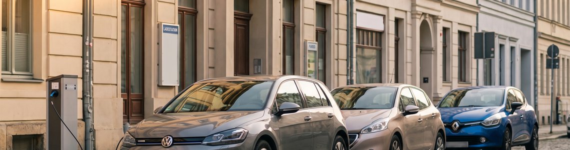 Innerstädtische Straße mit Altbauten, am Rand parkende Autos und ein Elektroauto an einer Ladesäule