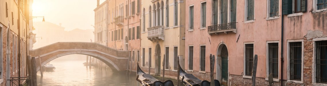 Ruhiger Kanal in Venedig am Morgen mit Palazzi, zwei Gondeln und einer Steinbrücke