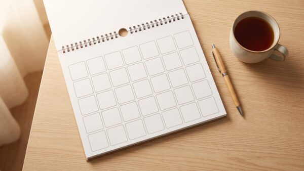 Aufgeschlagener Kalender mit leeren Feldern neben Stift und Tee
