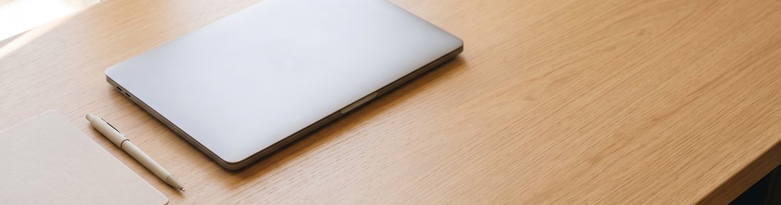 Zugeklappter Laptop neben einem geschlossenen Notizbuch auf einem hellen Holzschreibtisch