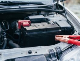 Starterbatterie im geöffneten Motorraum mit einer roten Starthilfeklemme daneben