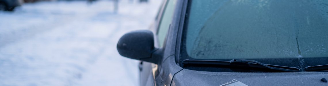 Vereiste Windschutzscheibe mit Eiskratzer auf der Motorhaube im winterlichen Morgenlicht