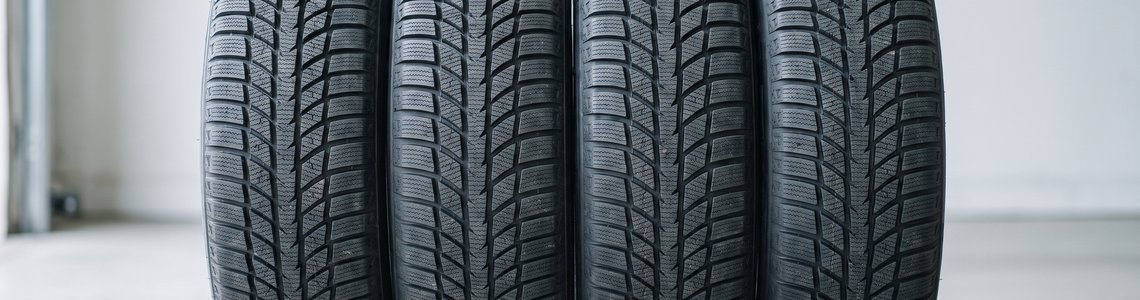 Vier neue Winterreifen mit unbeschrifteten Flanken nebeneinander auf einem Werkstattboden