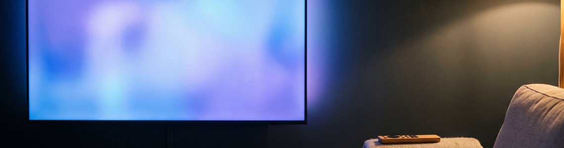 Wohnzimmer am Abend mit großem Fernseher, Sideboard und Sofaecke mit Fernbedienung