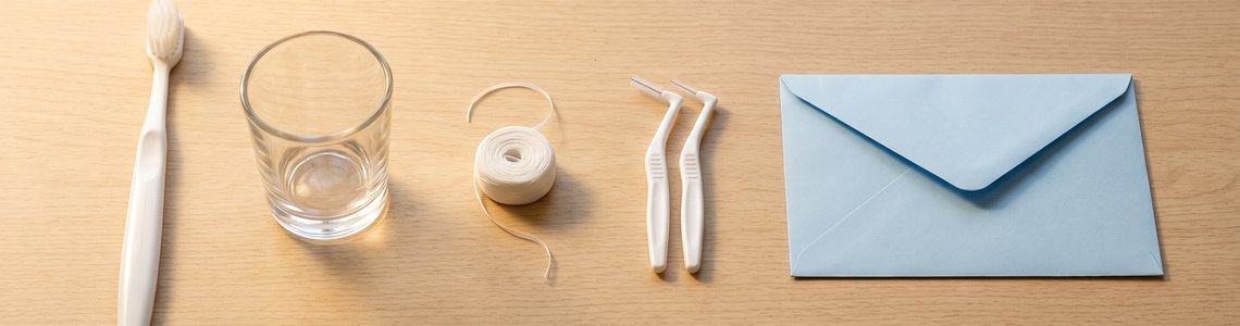 Zahnbürste, Glasbecher, Zahnseide und Interdentalbürsten auf einem hellen Holztisch