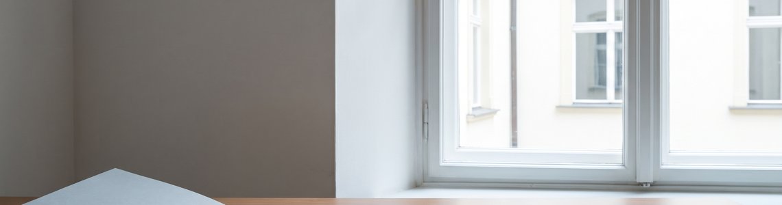 Aufgeschlagener Aktenordner und Papierstapel auf einem Schreibtisch vor einem hellen Sprossenfenster