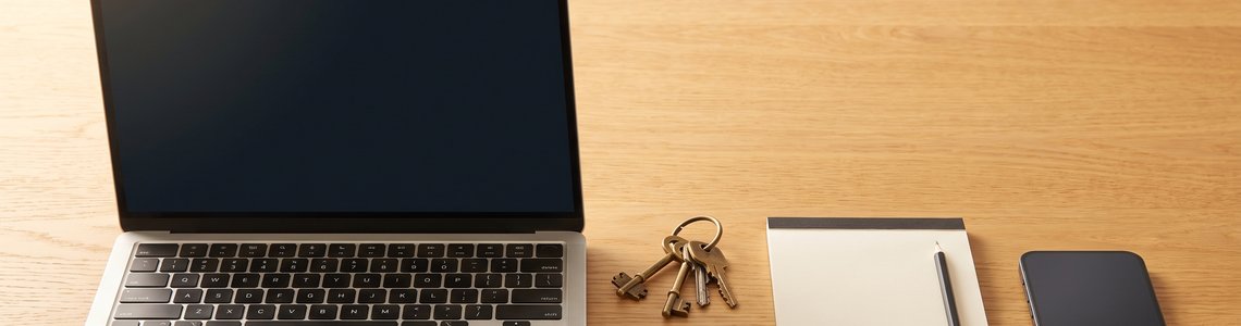 Schreibtisch mit Laptop, Schlüsselbund, Sicherheitsschlüssel, Notizbuch und Smartphone im warmen Tageslicht