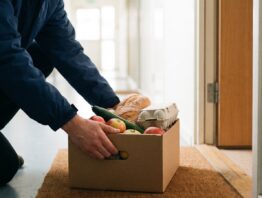 Lieferfahrer stellt eine Kiste mit Lebensmitteln vor eine Wohnungstür