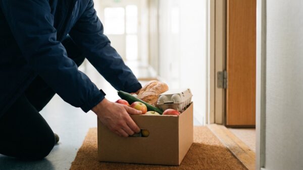 Lieferfahrer stellt eine Kiste mit Lebensmitteln vor eine Wohnungstür