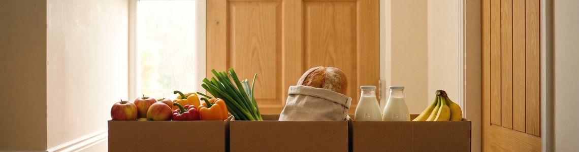 Lieferkisten mit Obst, Gemüse, Brot und Milch vor einer Wohnungstür