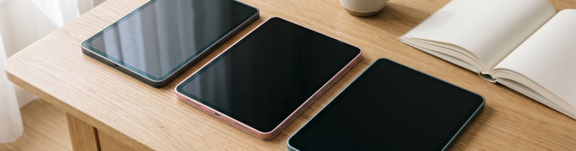 Drei Tablets in verschiedenen Größen und Farben auf einem Holztisch