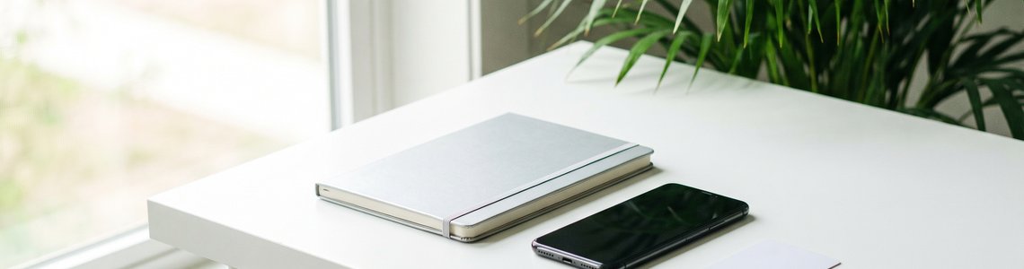 Heller Schreibtisch mit Notebook, Smartphone und einer unbedruckten Karte am Fenster