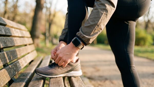 Handgelenk mit Smartwatch beim Schnüren eines Laufschuhs auf einer Parkbank