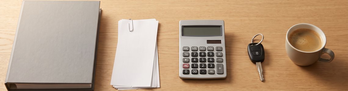 Schreibtisch mit Aktenordner, unbeschrifteten Belegen, Taschenrechner, Autoschlüssel und Kaffeetasse