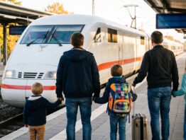 Familie mit zwei Kindern wartet am Bahnsteig auf einen einfahrenden weißen Schnellzug