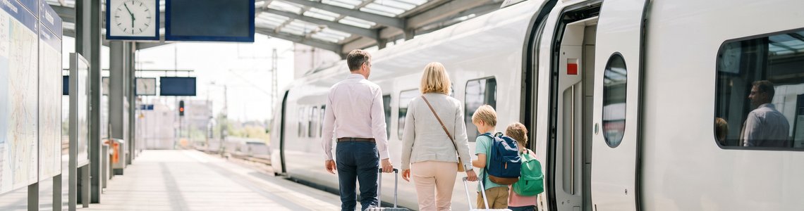 Familie mit zwei Kindern und Koffern geht am Bahnsteig auf einen weißen Schnellzug zu