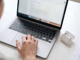 bookbeat kuendigen bild 1 Hand am Touchpad eines Laptops, daneben kabellose Kopfhörer im geöffneten Ladeetui