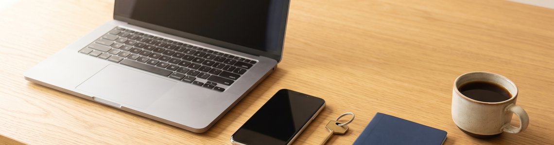 Laptop, Smartphone, Schlüsselbund, Autoschlüssel und Kaffeetasse auf einem hellen Holzschreibtisch