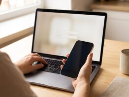 Hände an Laptop und Smartphone bei der Anmeldung im Online-Banking am Küchentisch