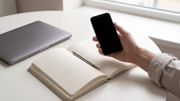 Hand mit Smartphone neben einem zugeklappten Laptop als Sinnbild für den Wechsel vom Browser zur App