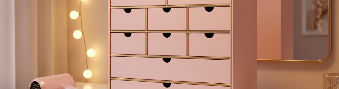 Rosafarbener Adventskalender mit Schubladen, Reisehaartrockner und Haarbürste auf einem Schminktisch