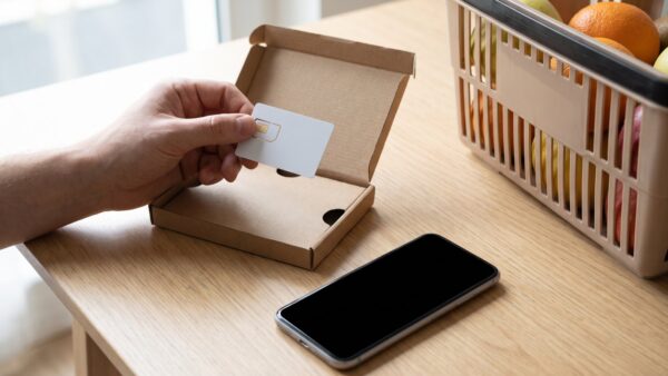 SIM-Karte aus einem Prepaid-Starterset über einem Smartphone und Einkaufskorb