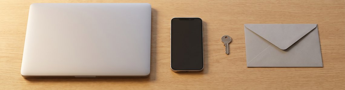 Laptop, Smartphone, Schlüssel und Briefumschlag auf einem hellen Holzschreibtisch