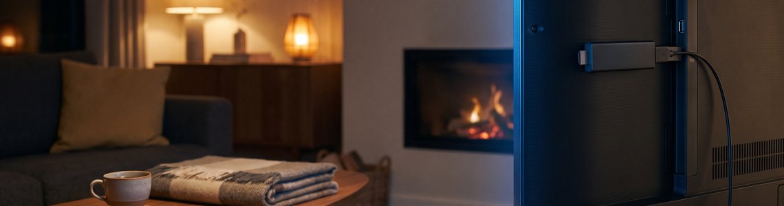 Kleiner Streaming-Stick hinter einem Fernseher, Fernbedienung auf dem Sofatisch
