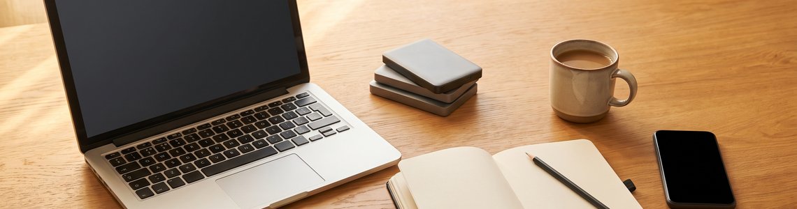 Schreibtisch mit Laptop, externen Festplatten, Notizbuch und Smartphone im warmen Tageslicht