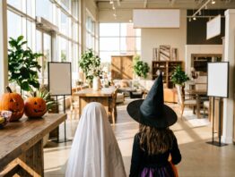 ikea halloween bild 1 Zwei verkleidete Kinder von hinten im Eingangsbereich eines Möbelhauses, daneben ein Tisch mit Süßigkeiten und Kürbissen