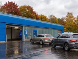 Einfahrt einer Autowaschstraße mit blauer Fassade, davor zwei wartende Autos auf nassem Asphalt