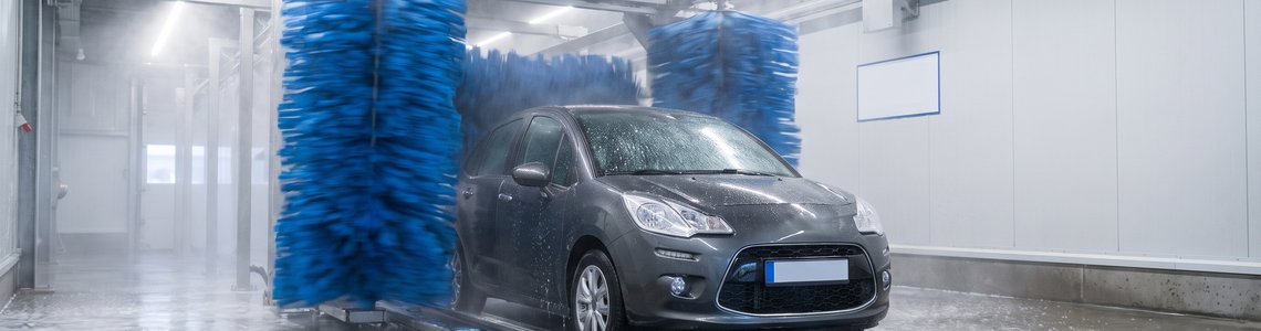 Kompaktwagen fährt auf dem Förderband durch die Schaumstoffwalzen einer Autowaschstraße