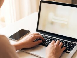 Hand an einer Laptop-Tastatur mit Smartphone daneben bei der Anmeldung im Online-Banking