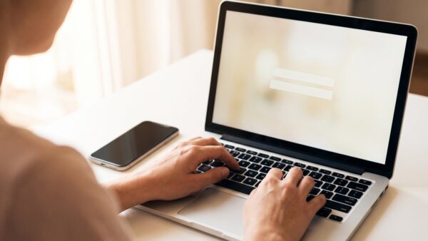 ing login bild 1 Hand an einer Laptop-Tastatur mit Smartphone daneben bei der Anmeldung im Online-Banking