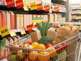 Einkaufswagen mit Obst und Gemüse vor einem Supermarktregal mit Aktionsschildern