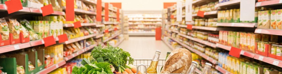 Einkaufswagen in einem Supermarktgang mit roten Aktionsschildern an den Regalen