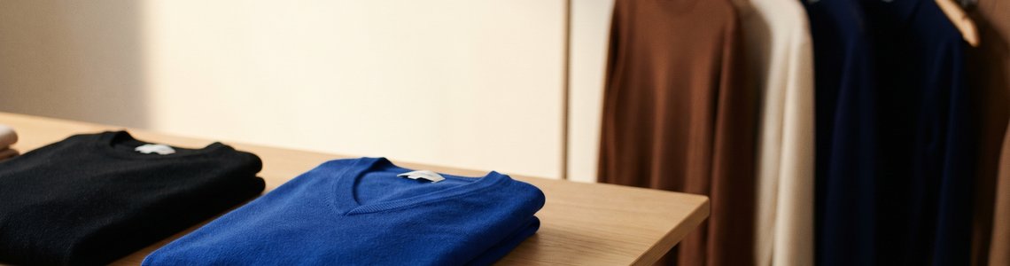 Gefalteter royalblauer Kaschmirpullover mit V-Ausschnitt neben schwarzem Pullover und Kleiderstange mit Herbstmode