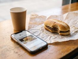 Smartphone mit unscharfem Newsletter neben einem länglichen Burger auf Einwickelpapier