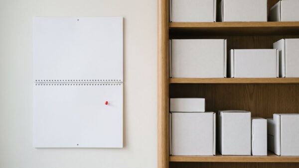 Unbeschrifteter Wandkalender mit roter Pinnnadel neben einem Regal mit verpackten Elektronikgeräten