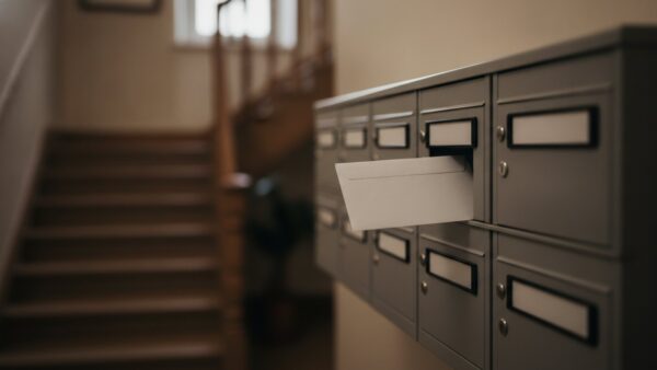 Briefkastenreihe im Hausflur, aus einem Schlitz ragt ein unbeschrifteter weißer Umschlag