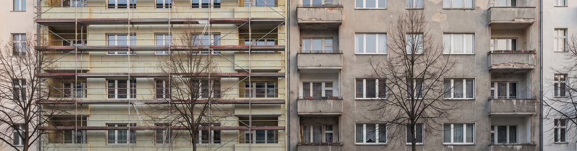 Mietshaus mit Baugerüst, eine Fassadenhälfte bereits gedämmt, die andere noch mit altem Putz