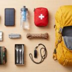 Inhalt eines Notfallrucksacks in der Draufsicht: Kurbelradio, Powerbank, Trinkflasche, Verbandtasche, Taschenkocher, Multitool und Regenponcho