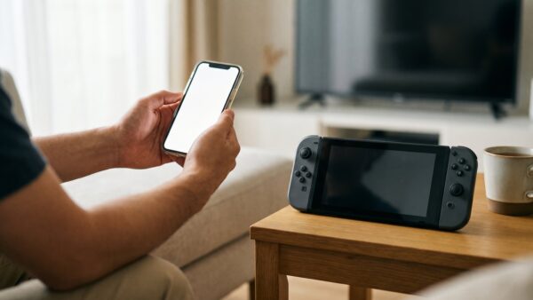 Hände halten ein Smartphone zur Anmeldung neben einer tragbaren Spielkonsole auf dem Couchtisch