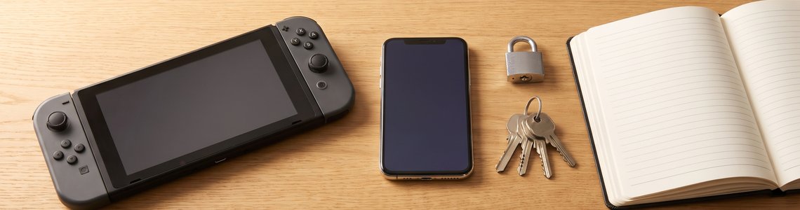 Tragbare Spielkonsole, Smartphone, Vorhängeschloss und Schlüssel auf einem Holzschreibtisch