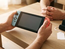 Hände halten eine Hybrid-Spielkonsole mit blauem und rotem Controller, daneben ein leeres Preisschild